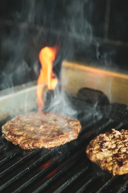 Burger patties sizzling on commercial grill generating grease that flows to trap below